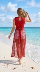Woman in a red lace dress standing on a beach with turquoise water and white clouds.