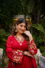 Woman in a red traditional outfit with floral patterns standing outdoors.