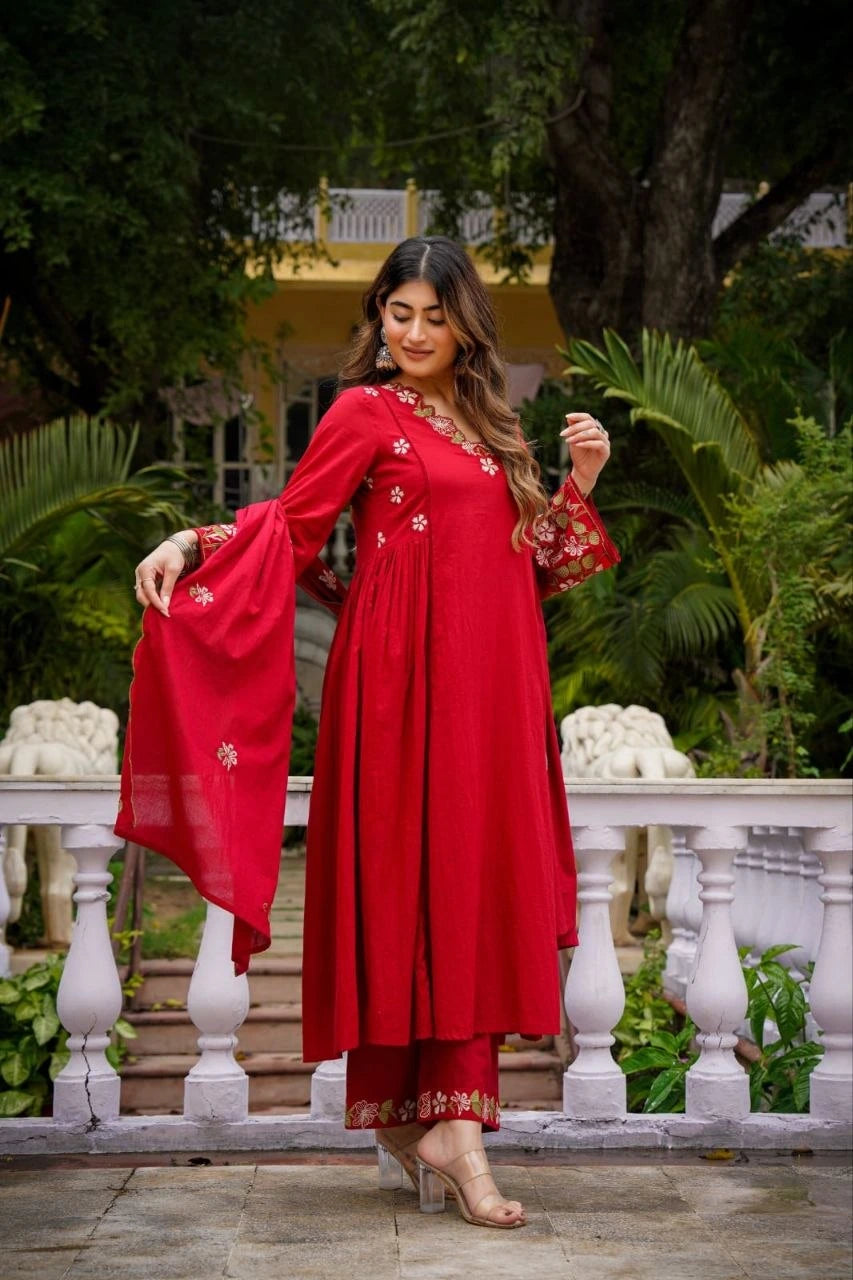 Woman in a red traditional outfit with floral embroidery standing outdoors.