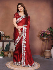 Woman in a red saree with white floral patterns standing in a decorated room.