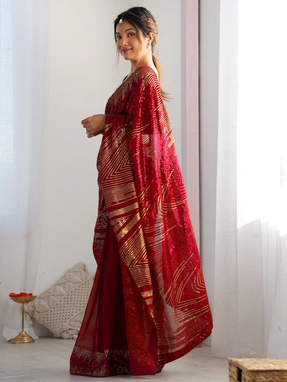 Woman wearing a red saree with white patterns in a minimal indoor setting