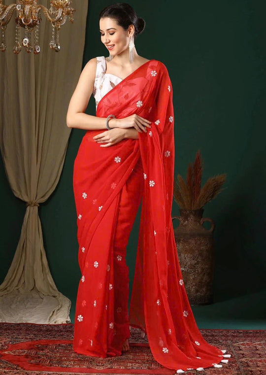 Woman wearing a red saree with white patterns against a green curtain background