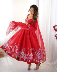 Woman in a red floral dress posing in a bright room with white curtains.