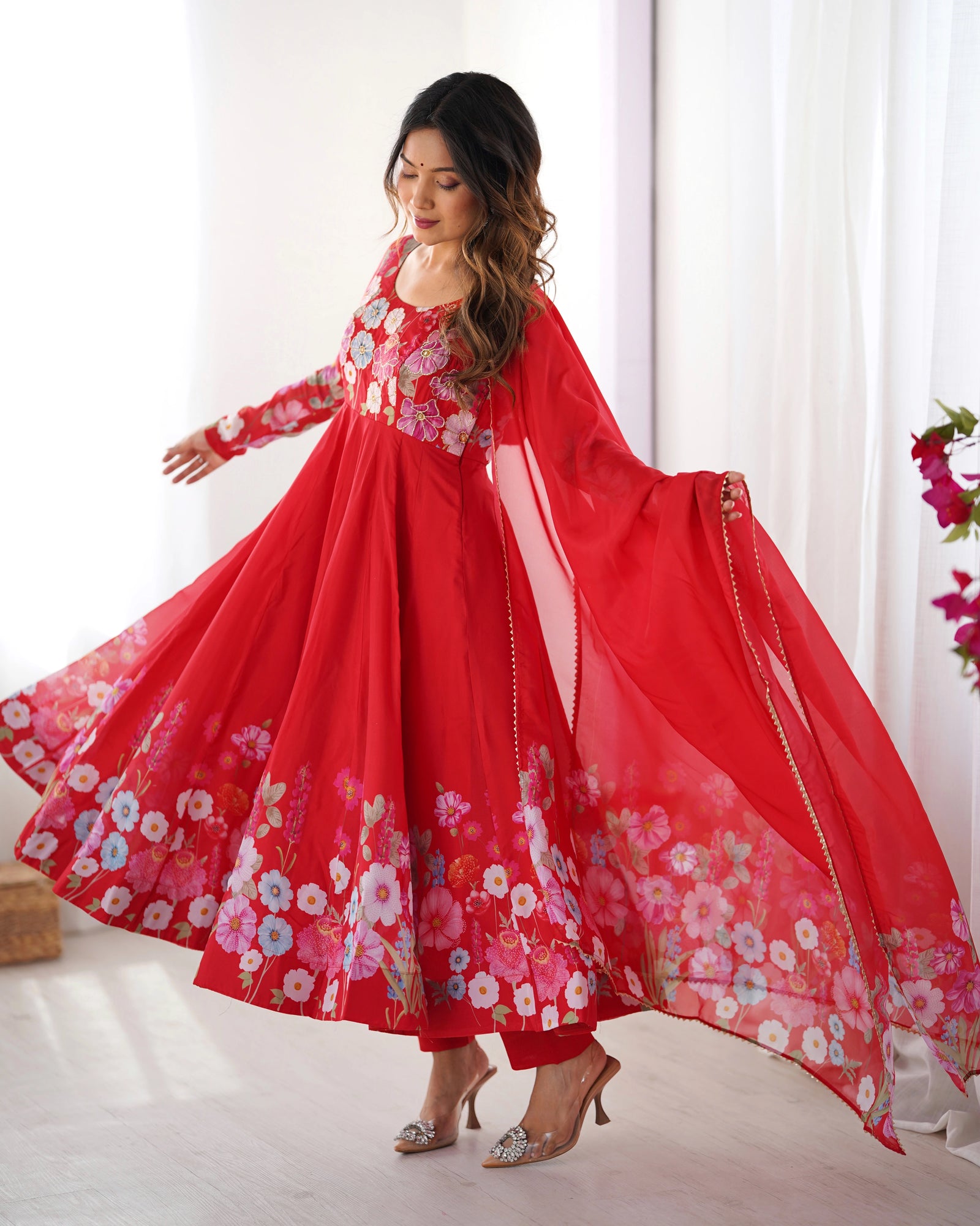 Woman wearing a red floral dress with a flowing skirt in a bright room.