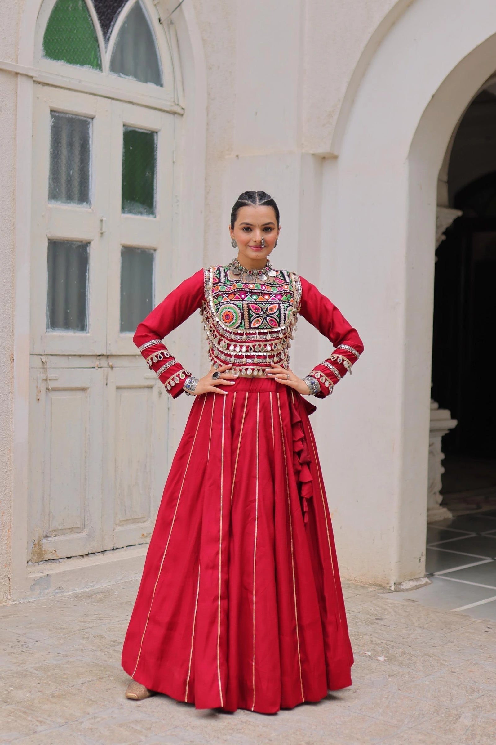 Woman in traditional red and embroidered outfit standing in front of a white building.