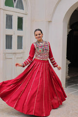 Woman in a traditional red outfit with intricate patterns standing in front of a white archway.