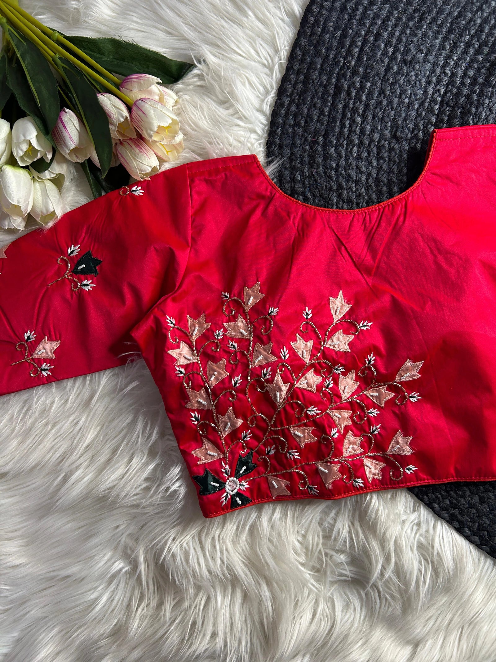 Red embroidered top on a white fur surface with flowers and a black knitted item.