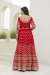 Woman wearing a red and white patterned outfit standing in front of a white architectural background.