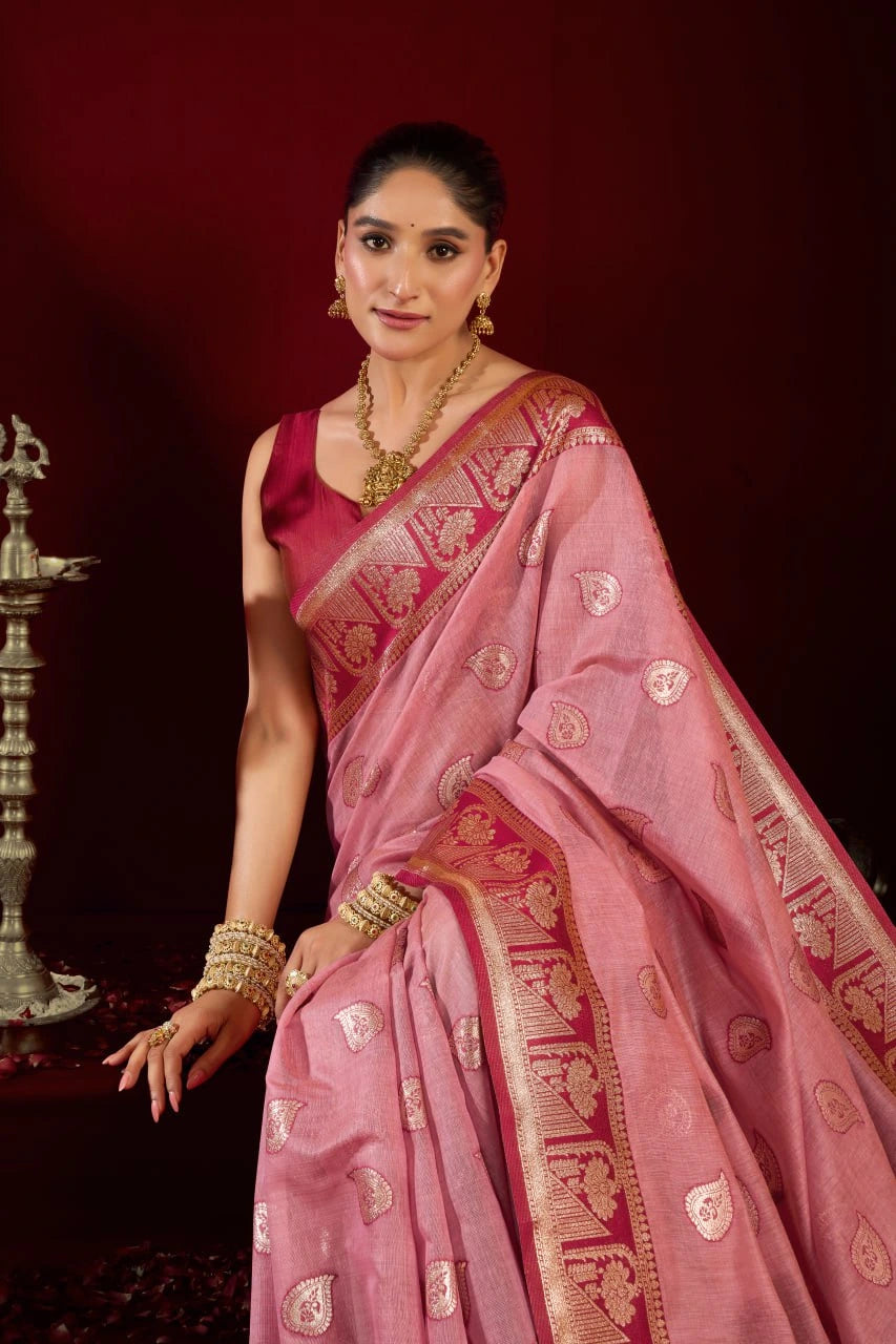 Woman in a pink saree with gold patterns against a dark background