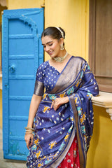 Woman wearing a blue saree with a colorful pattern in front of a blue door and yellow wall.