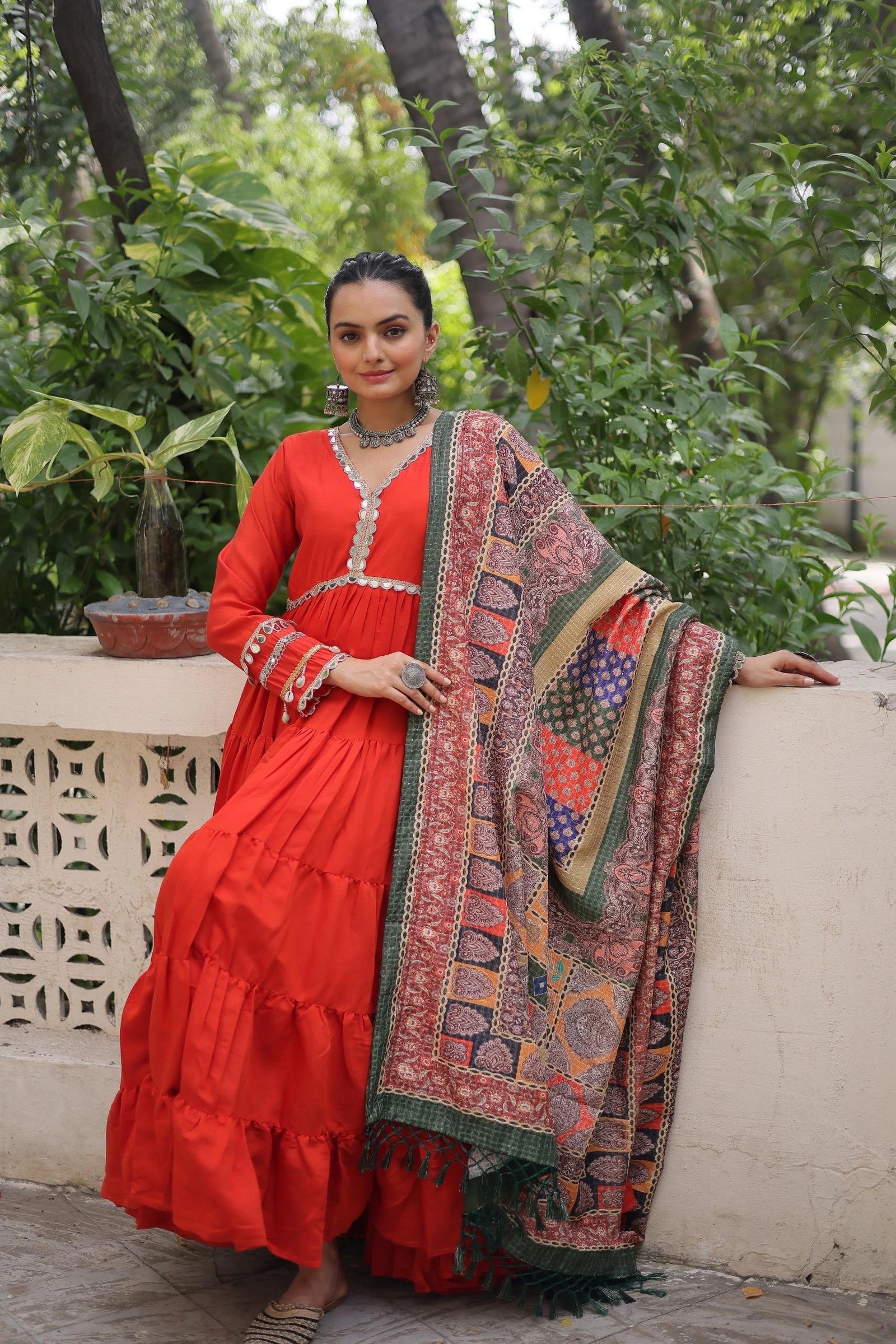 Woman in a red traditional outfit with a patterned shawl outdoors.