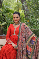 Woman in a red dress with a patterned shawl sitting outdoors.