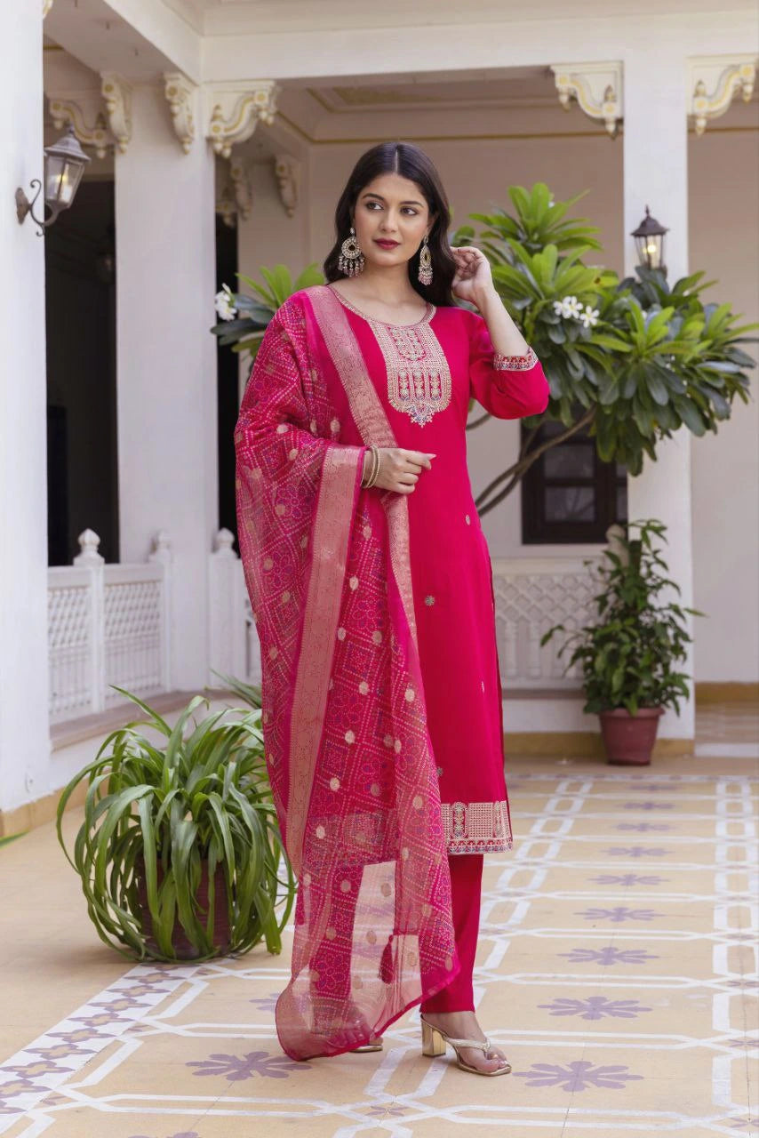 Woman in a bright pink traditional outfit with a matching dupatta standing in an elegant indoor setting.