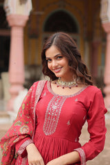 Woman in a red traditional outfit with intricate designs, standing in front of an architectural background.