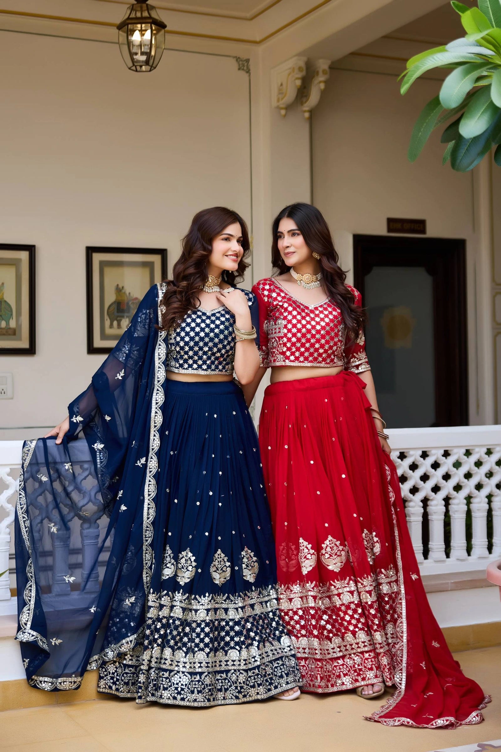 Two women in traditional blue and red sarees standing indoors.