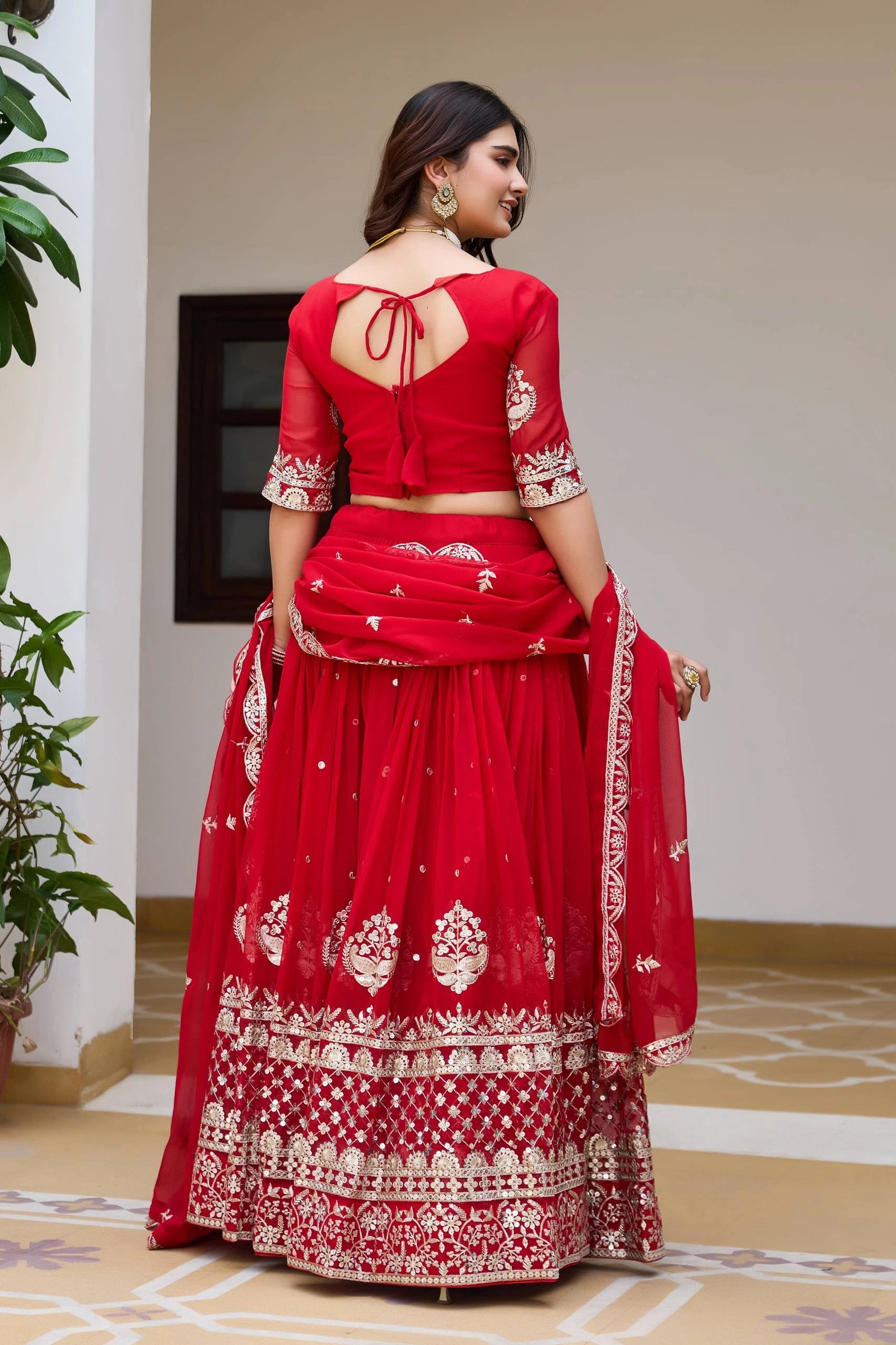 Woman wearing a red traditional outfit with white patterns indoors.