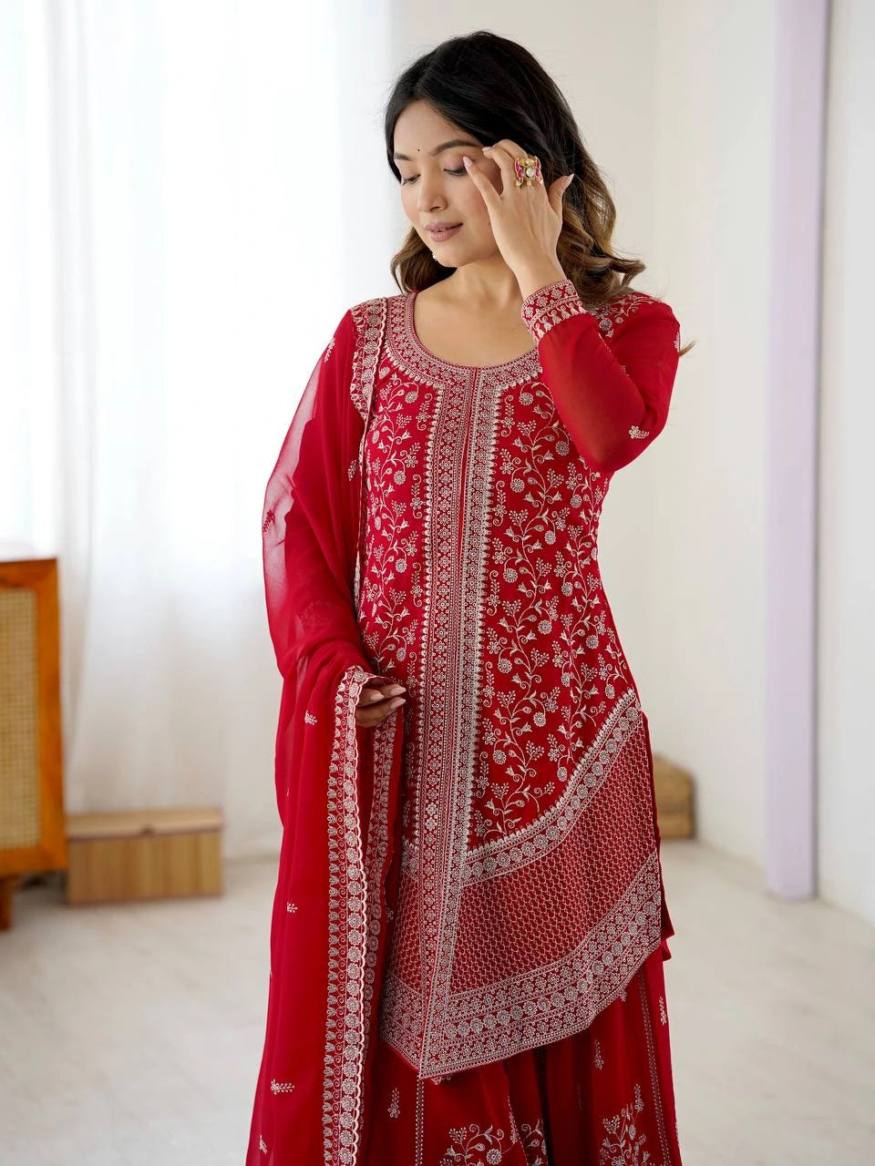 Woman wearing a red traditional outfit with white patterns in a minimalistic room.