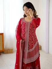 Woman wearing a red traditional outfit with white patterns in a minimalistic room.