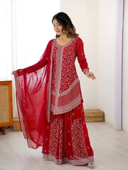 Woman wearing a red traditional outfit with white patterns in a minimalistic room.