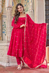 Woman in a red traditional outfit with a matching dupatta standing in front of an ornate wall.