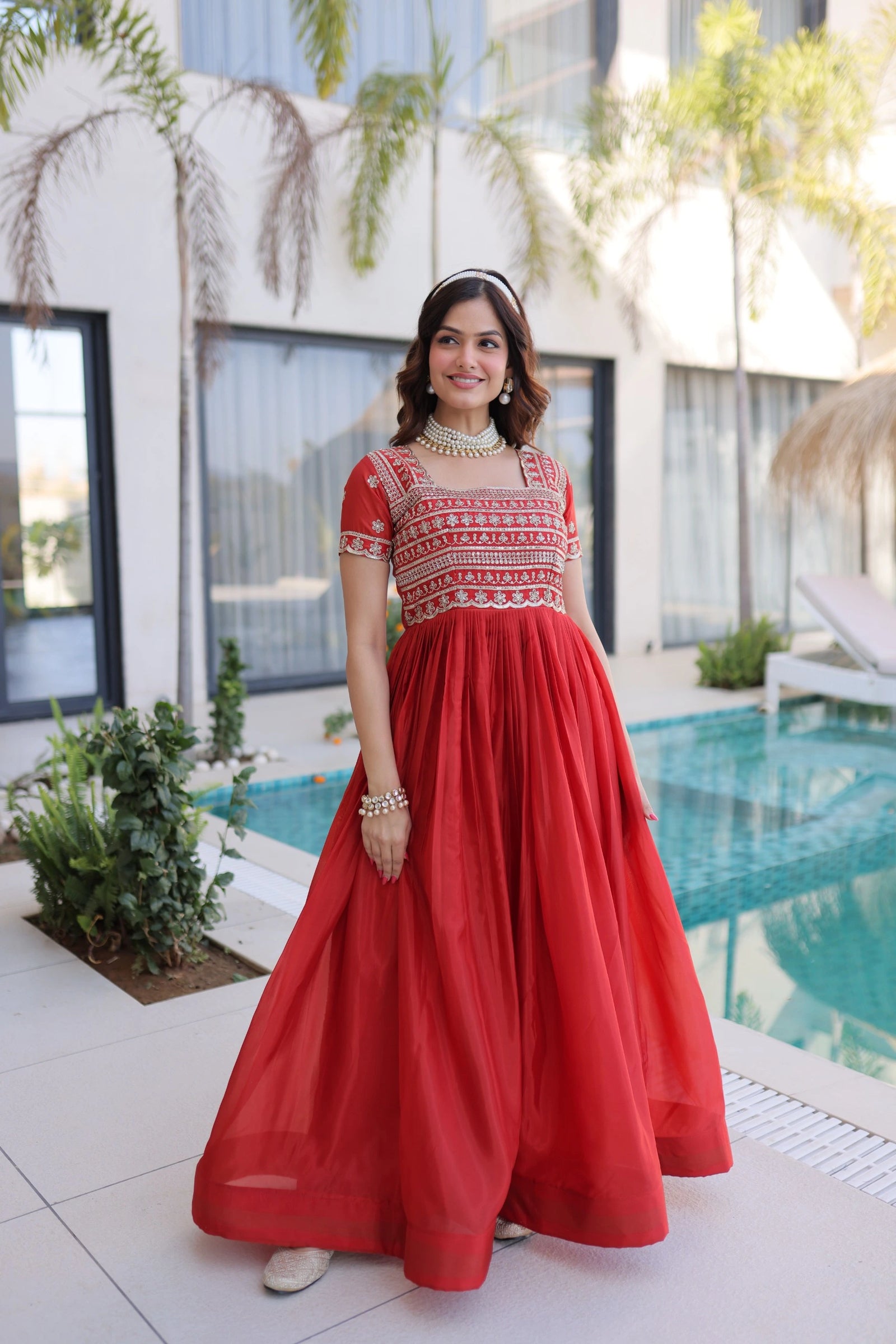 Woman in a red dress standing by a pool with a modern building in the background