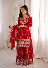 Woman wearing a red traditional outfit with white patterns in a bright room.