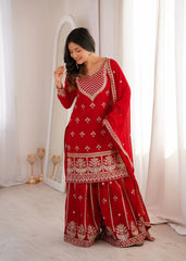 Woman in a red traditional outfit with white patterns standing in a well-lit room.