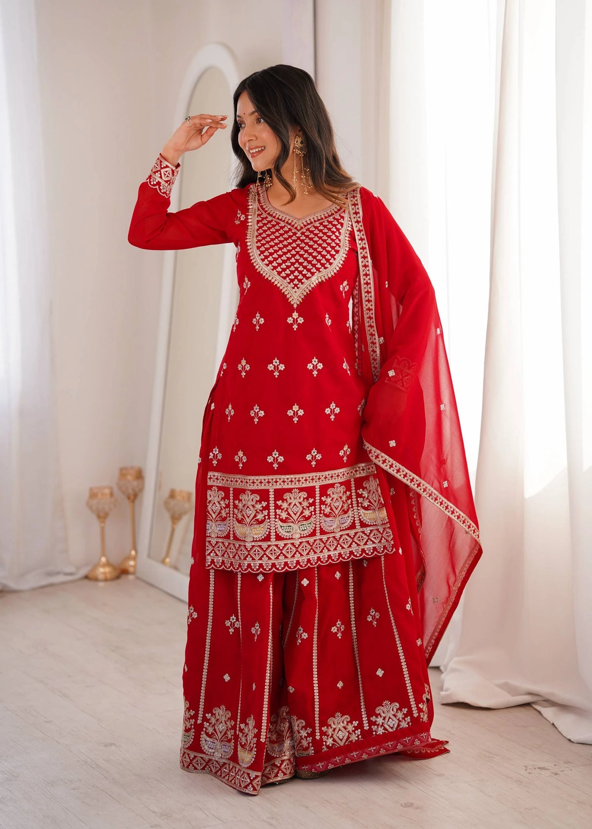 Woman in a red traditional outfit with white patterns standing in a well-lit room.