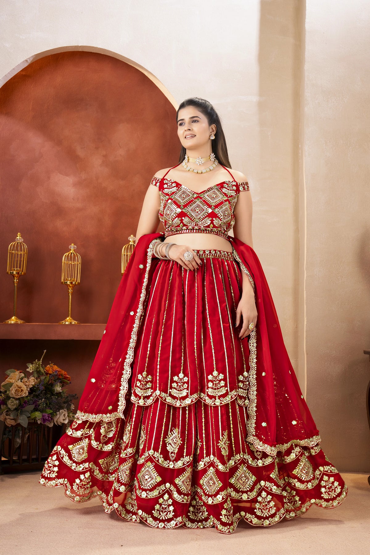 Woman in a red and gold embroidered traditional outfit standing against a neutral background
