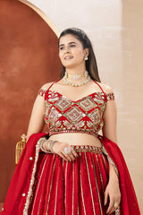 Woman in a red and gold traditional outfit with jewelry against a beige wall.