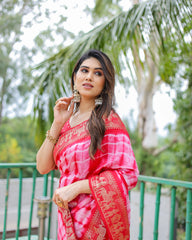 Woman in a pink saree with gold patterns standing outdoors with greenery in the background