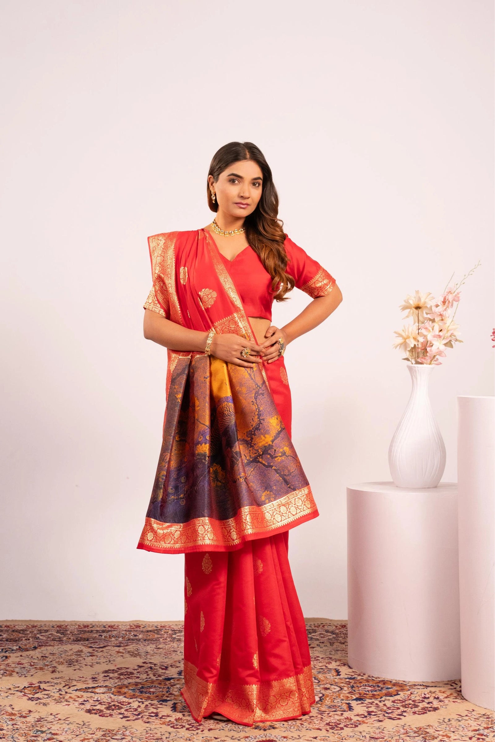 Woman wearing a red saree with a patterned blouse against a white background