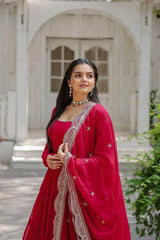 Woman in a red traditional outfit with intricate designs standing outdoors.