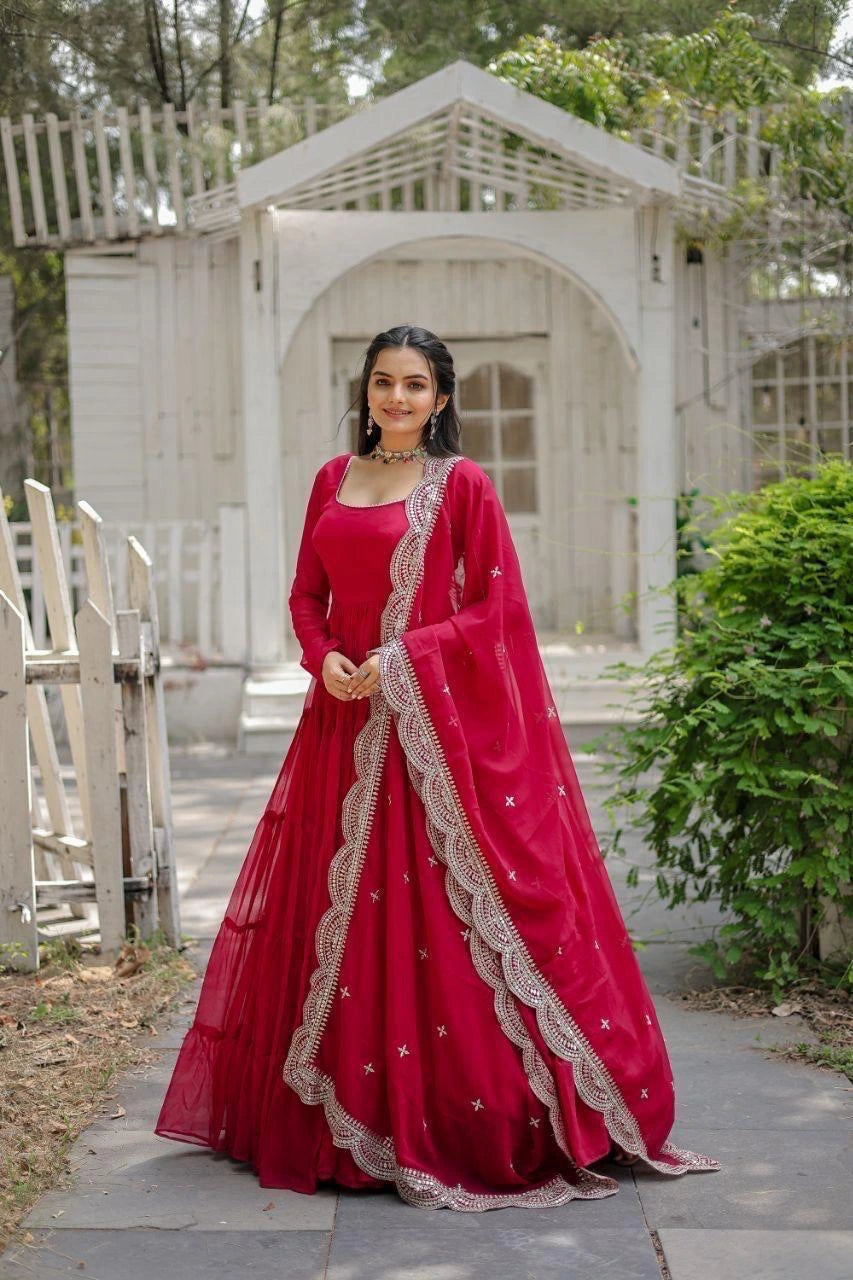 Woman in a red traditional outfit standing outdoors with greenery and a white structure in the background