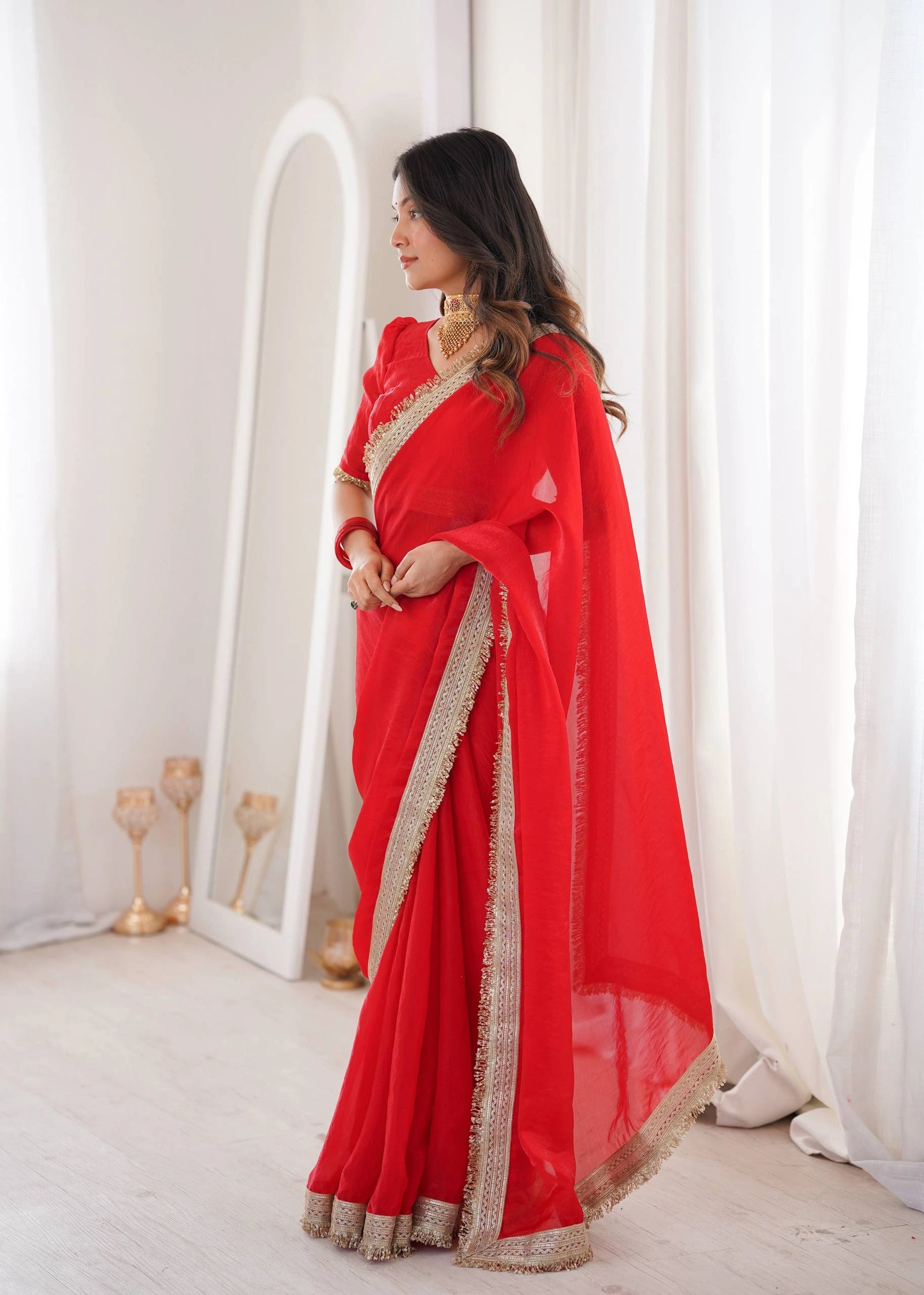 Woman wearing a red saree with gold border in a bright room.