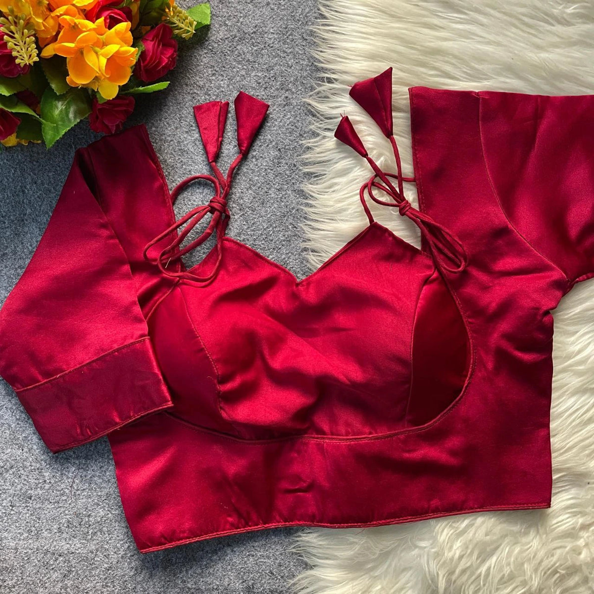 Red satin top with tie straps on a textured surface with flowers in the corner