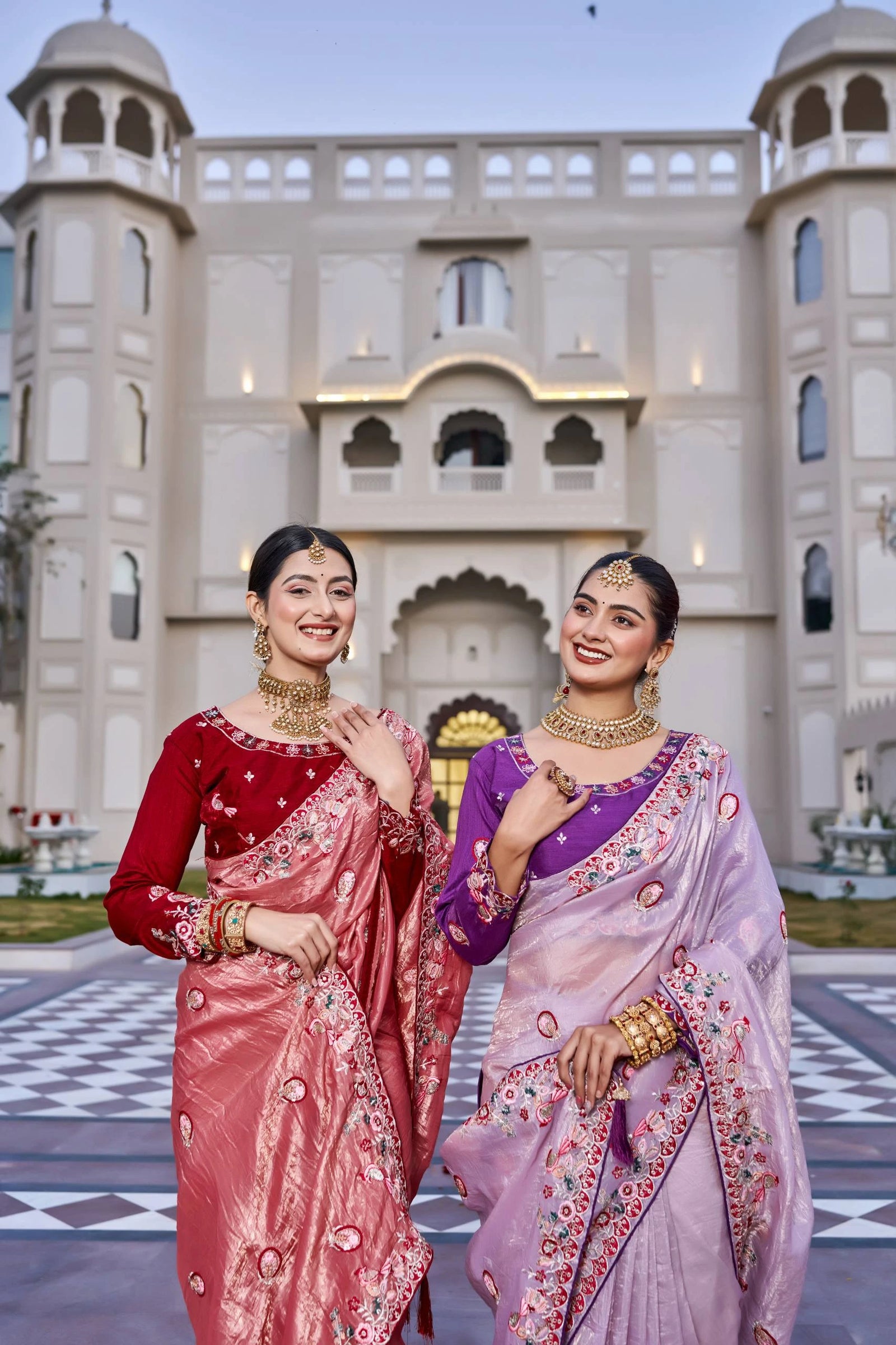 Two women in traditional sarees standing in front of a decorative building.
