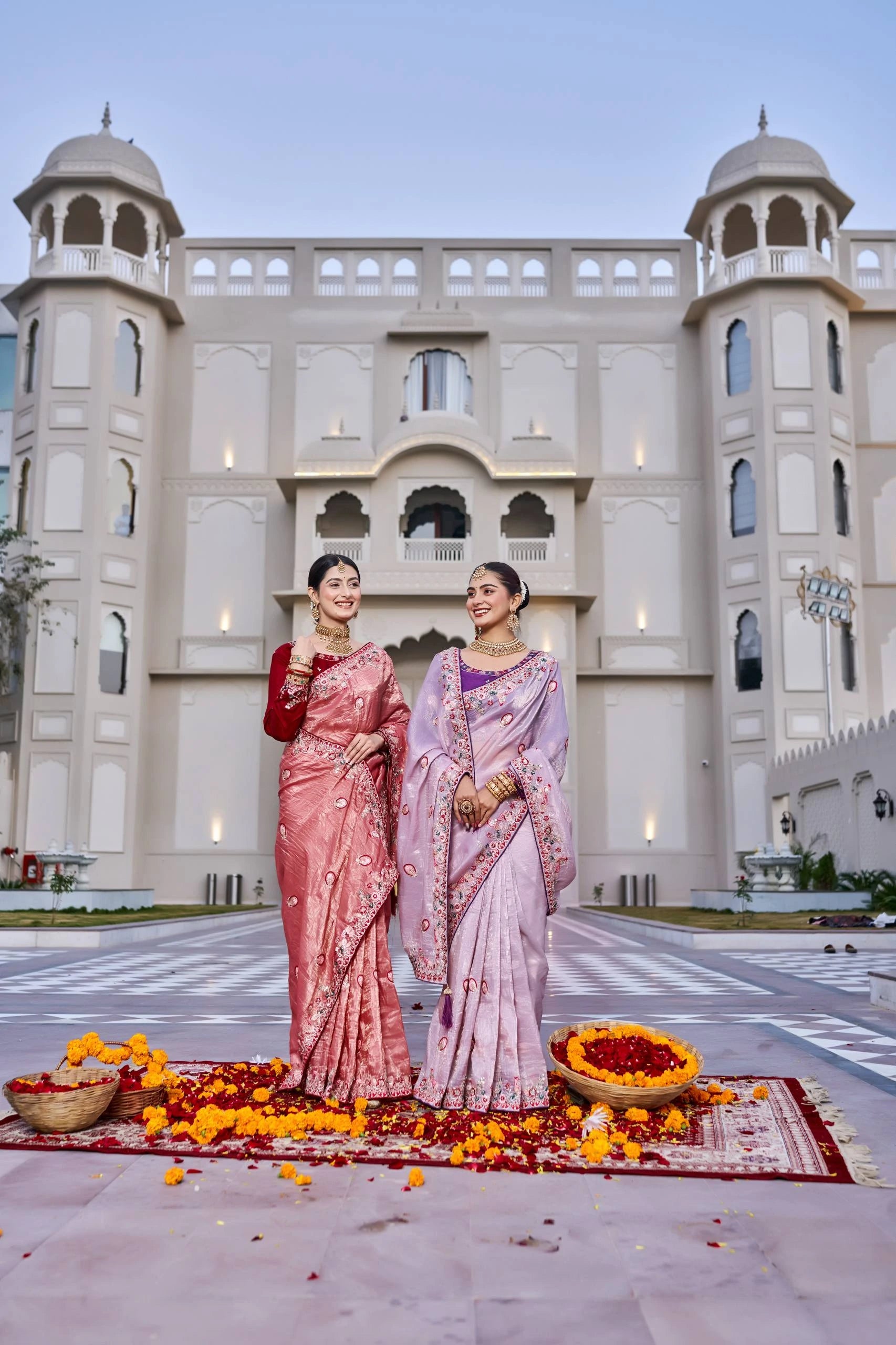 Two women in traditional sarees standing in front of a building with floral decorations.