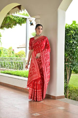 Woman in a red saree standing on a balcony with greenery in the background