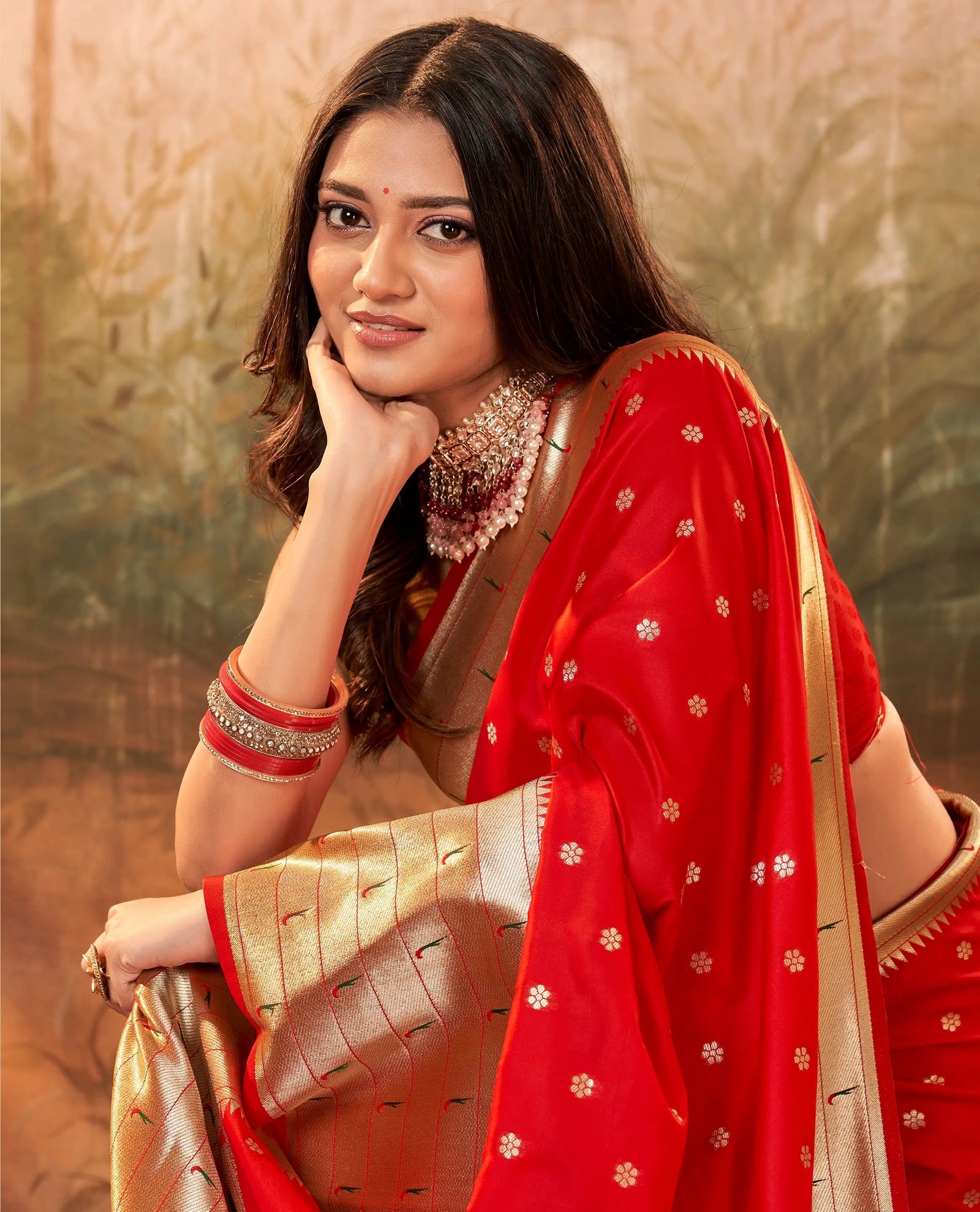 Woman wearing a red and gold saree with a blurred natural background