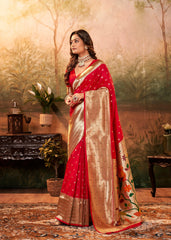 Woman in a red and gold saree standing in a decorated room with plants and furniture.