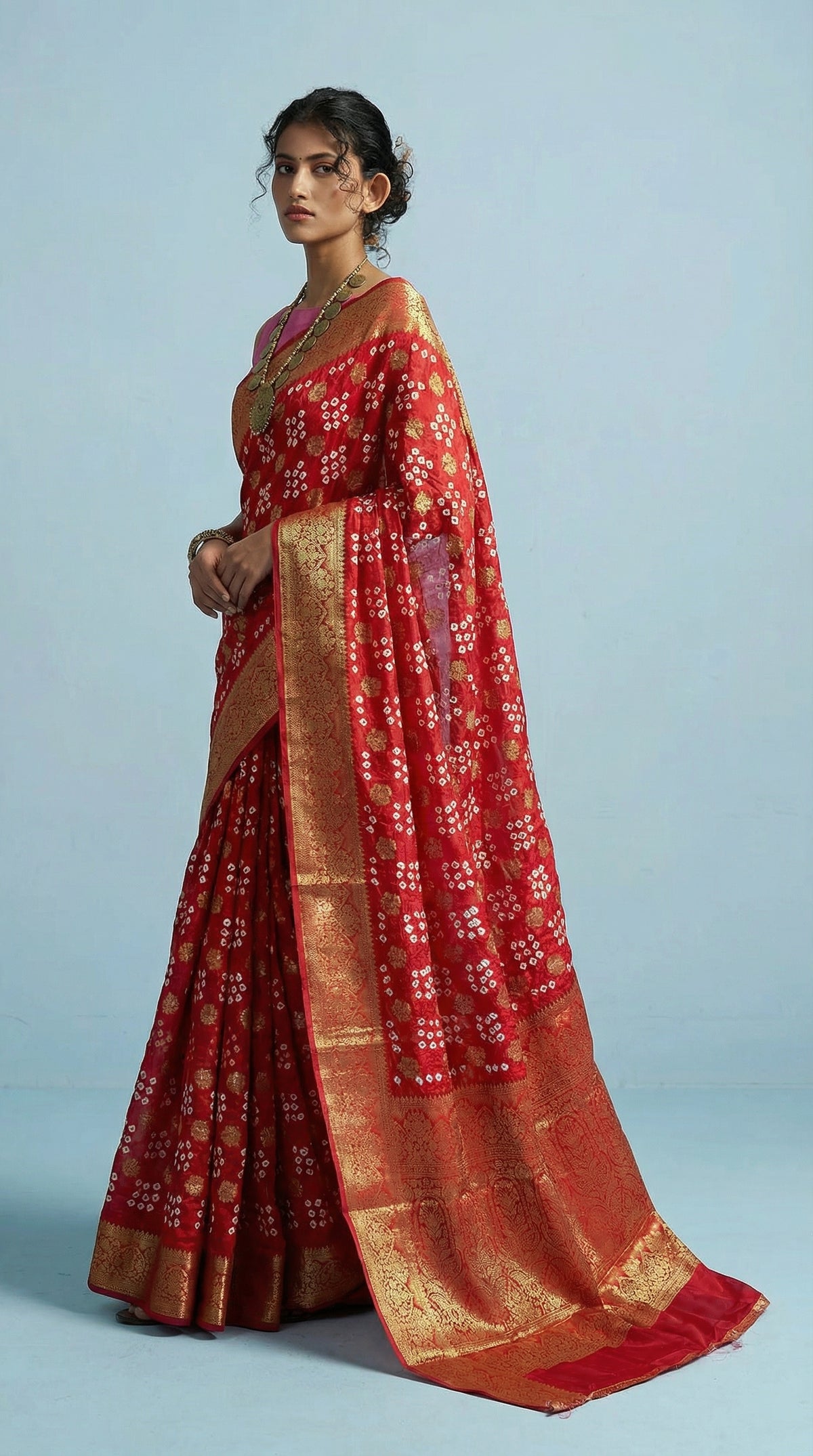Woman wearing a red saree with gold border on a light blue background