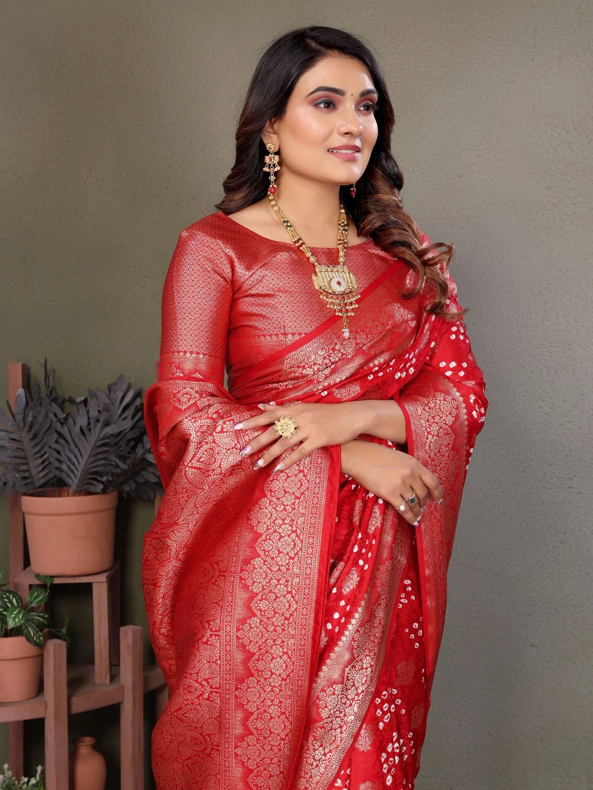 Woman wearing a red saree with gold patterns against a gray background