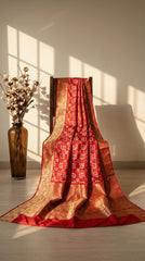 Red and gold saree draped over a chair with a vase of dried flowers in the background