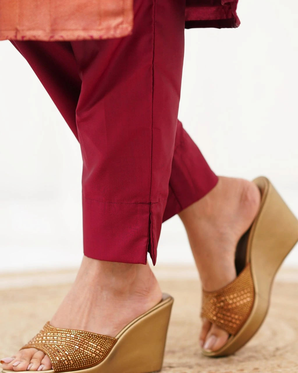 Close-up of feet wearing gold wedge sandals on a neutral background
