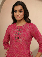 Woman wearing a pink embroidered traditional outfit against a beige background