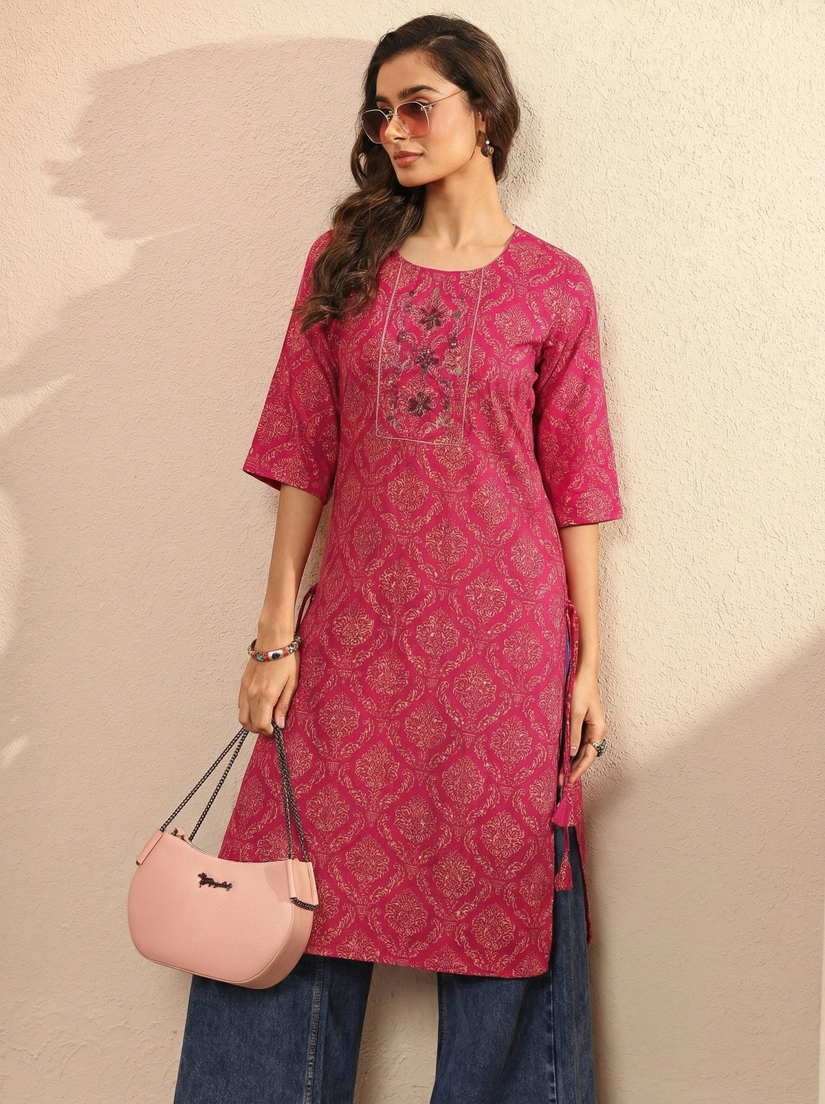 Woman wearing a pink patterned kurta with blue jeans against a beige background