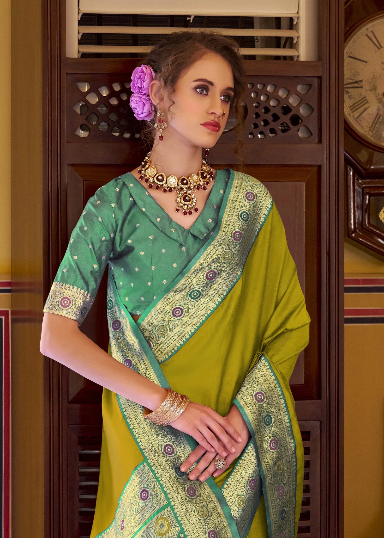 Woman wearing a green and yellow saree with jewelry in an indoor setting