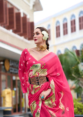 Woman in a pink saree with floral patterns standing in front of a building.