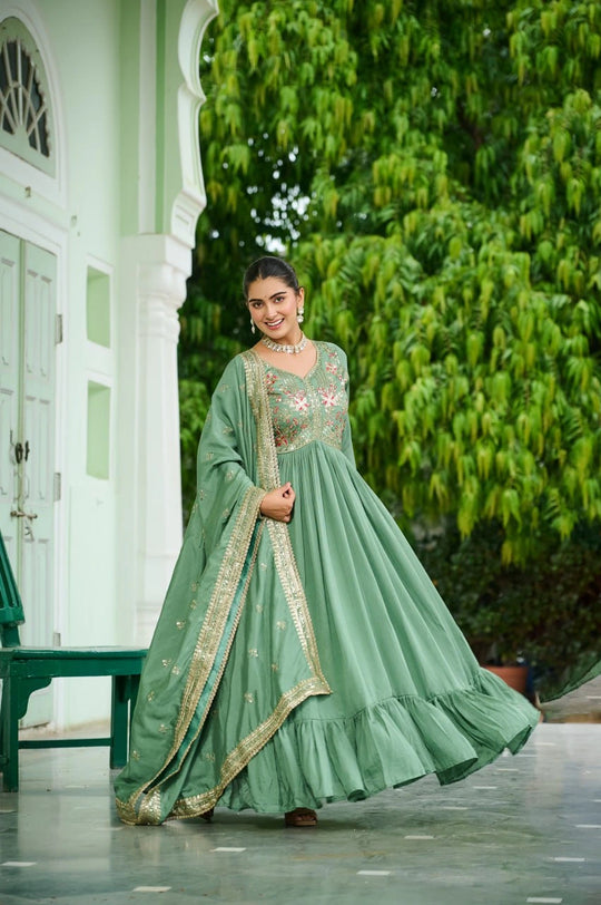 Woman in a green traditional outfit standing outdoors with greenery in the background